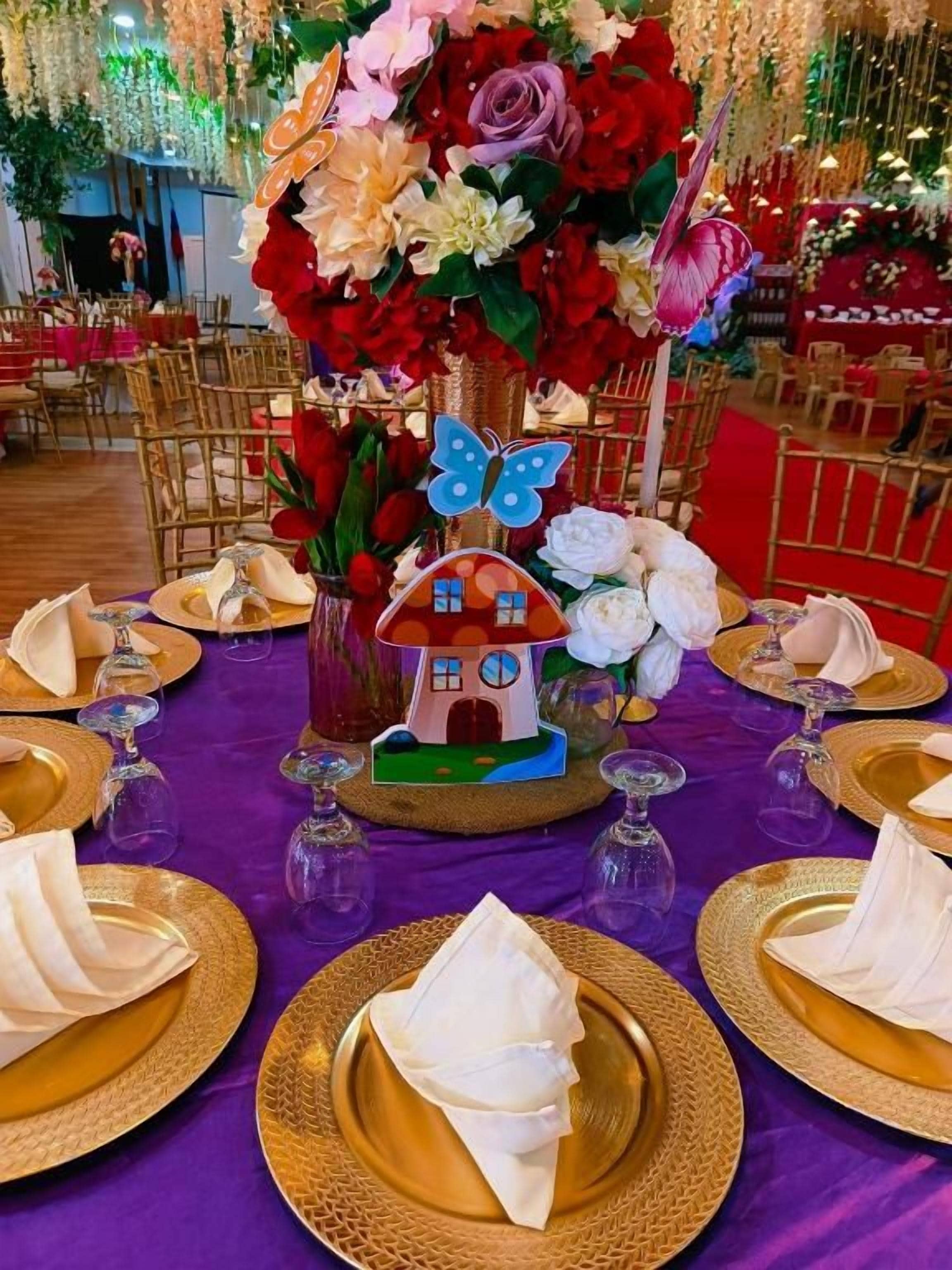 A table set with gold-rimmed plates, folded napkins, and a centerpiece with a house-shaped decoration and flowers.