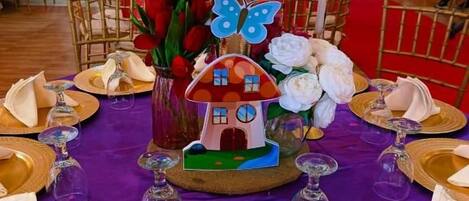 A table set with gold-rimmed plates, folded napkins, and a centerpiece with a house-shaped decoration and flowers.