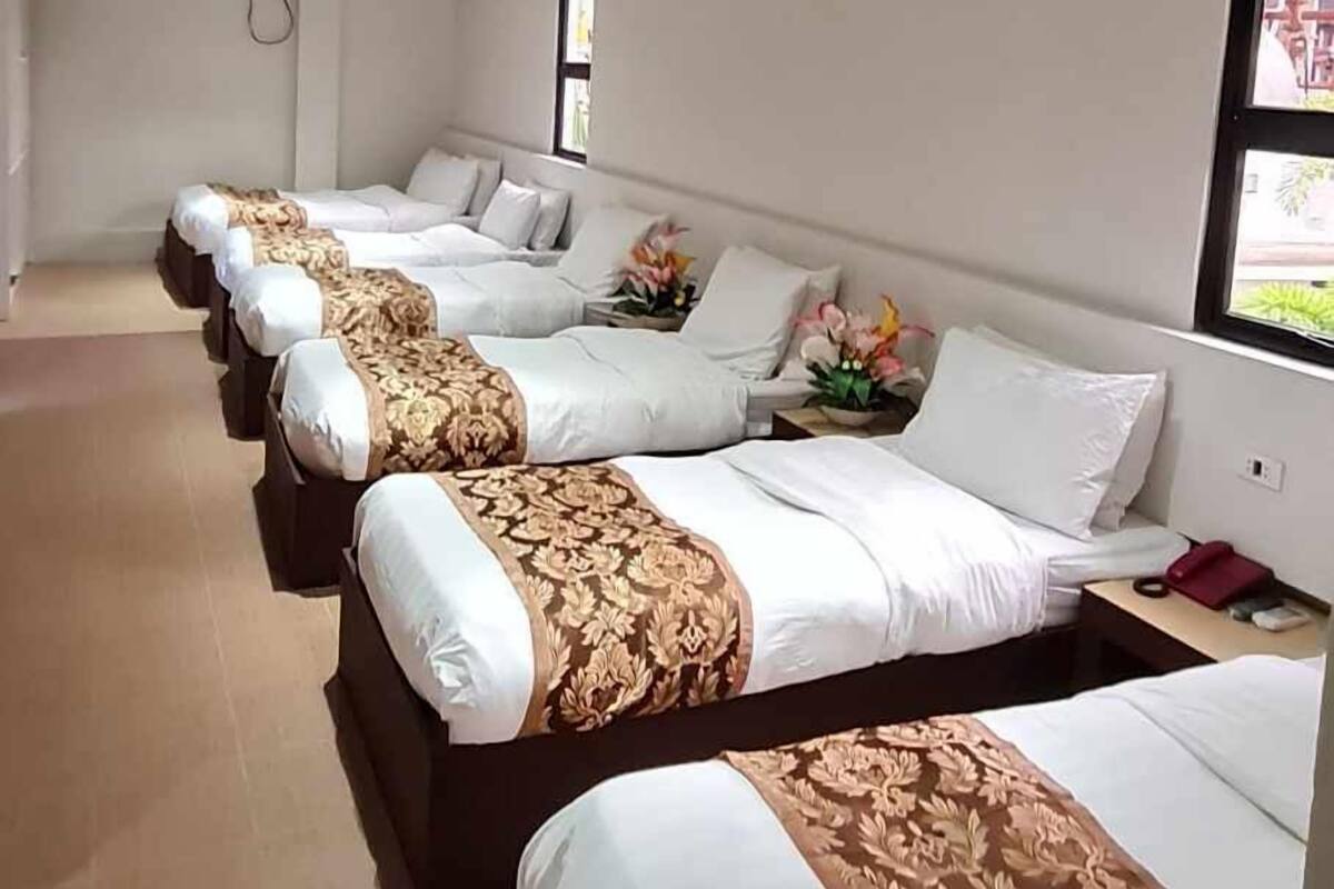 A hotel room with four beds arranged in a row, each with white bedding and decorative headboards.