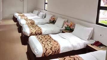 Ein Hotelzimmer mit vier Betten, die nebeneinander stehen, jeweils mit weißer Bettwäsche und dekorativen Kopfteilen.