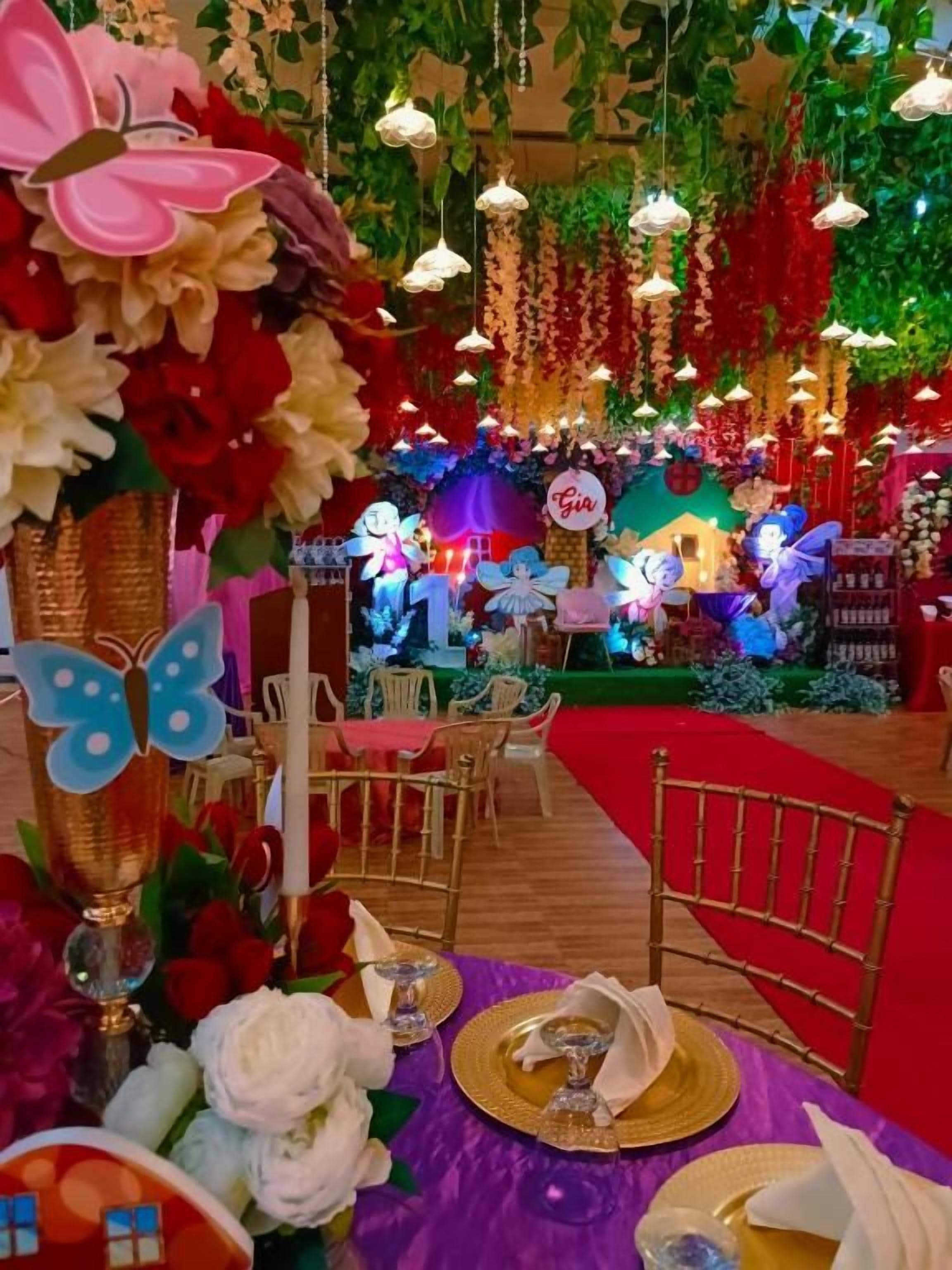 Un espace intérieur décoré, avec des tables dressées pour le repas, une scène où se produisent des artistes et des compositions florales suspendues.