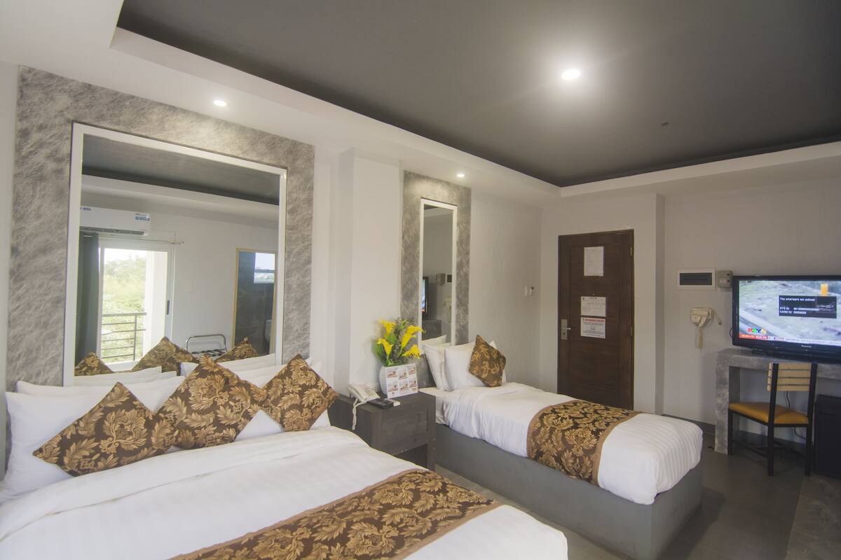 A hotel room with two beds, a large mirror, a desk with a chair, and a television.