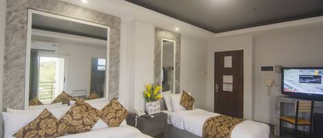 A hotel room with two beds, a large mirror, a desk with a chair, and a television.