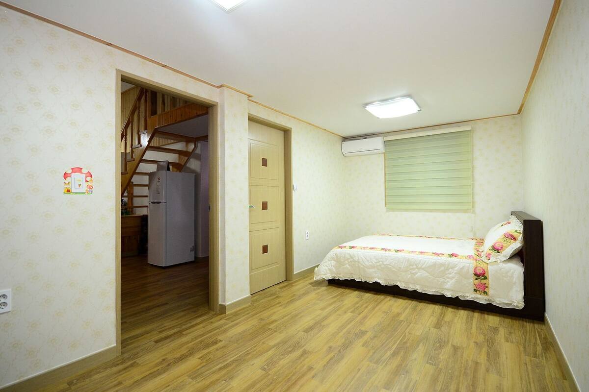 A bedroom with a bed, a wardrobe, a door leading to a staircase, and an air conditioning unit.