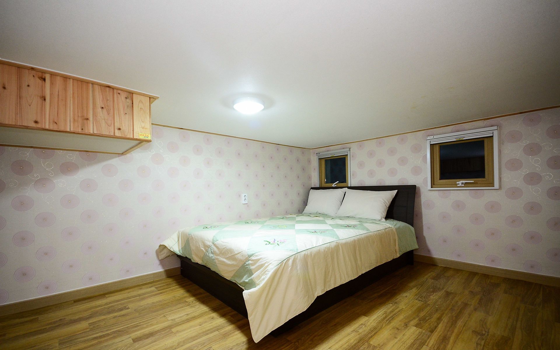 A bedroom with a bed, wooden flooring, a window, and a ceiling light.