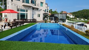A swimming pool with a tiled deck, surrounded by a well-maintained lawn and outdoor furniture. - Sun and Moon Pension (Yeosu)