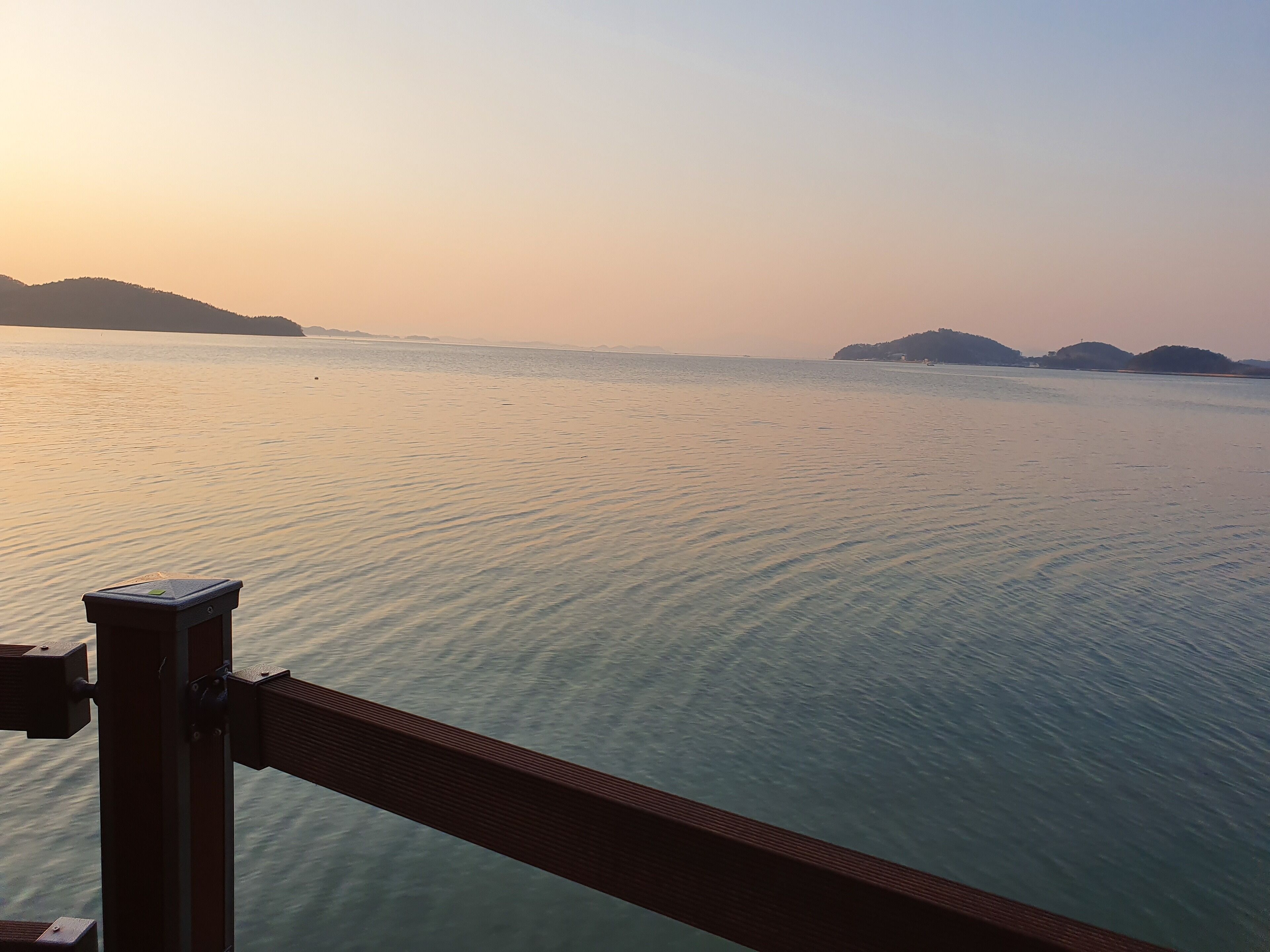 A calm body of water with distant landforms, viewed from a structure with a metal railing.