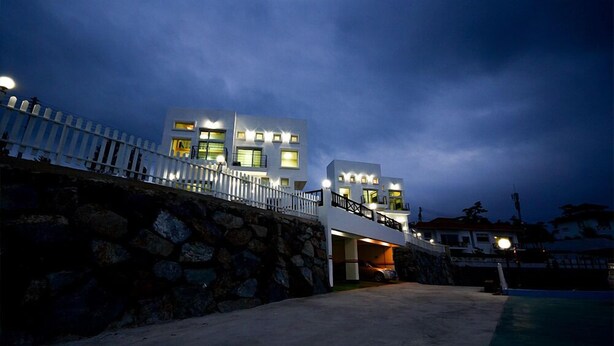 A modern two-story building with a stone retaining wall, a covered driveway, and a pool area. - Sun and Moon Pension (Yeosu)
