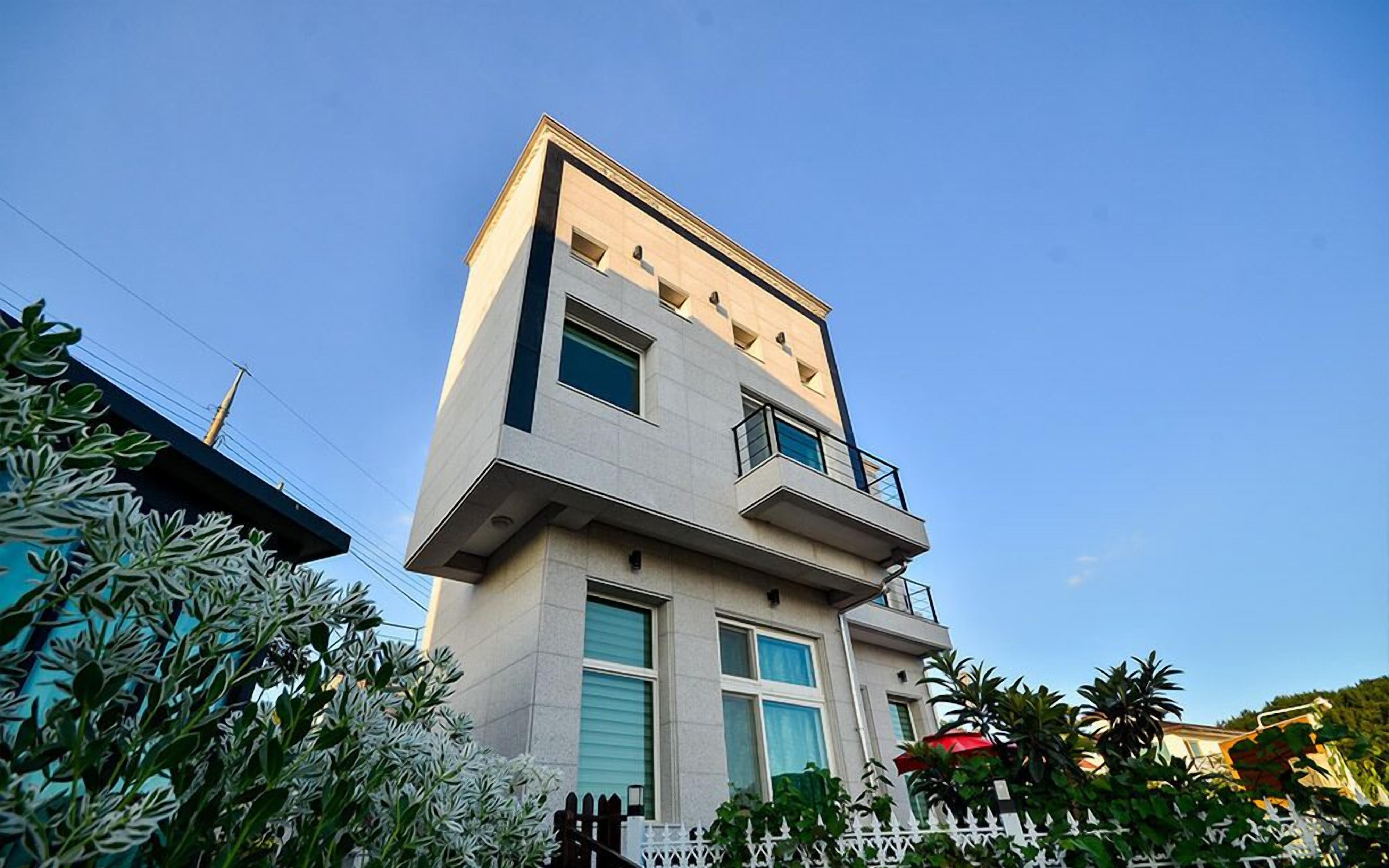 A modern two-story building with a flat roof, large windows, and a balcony.