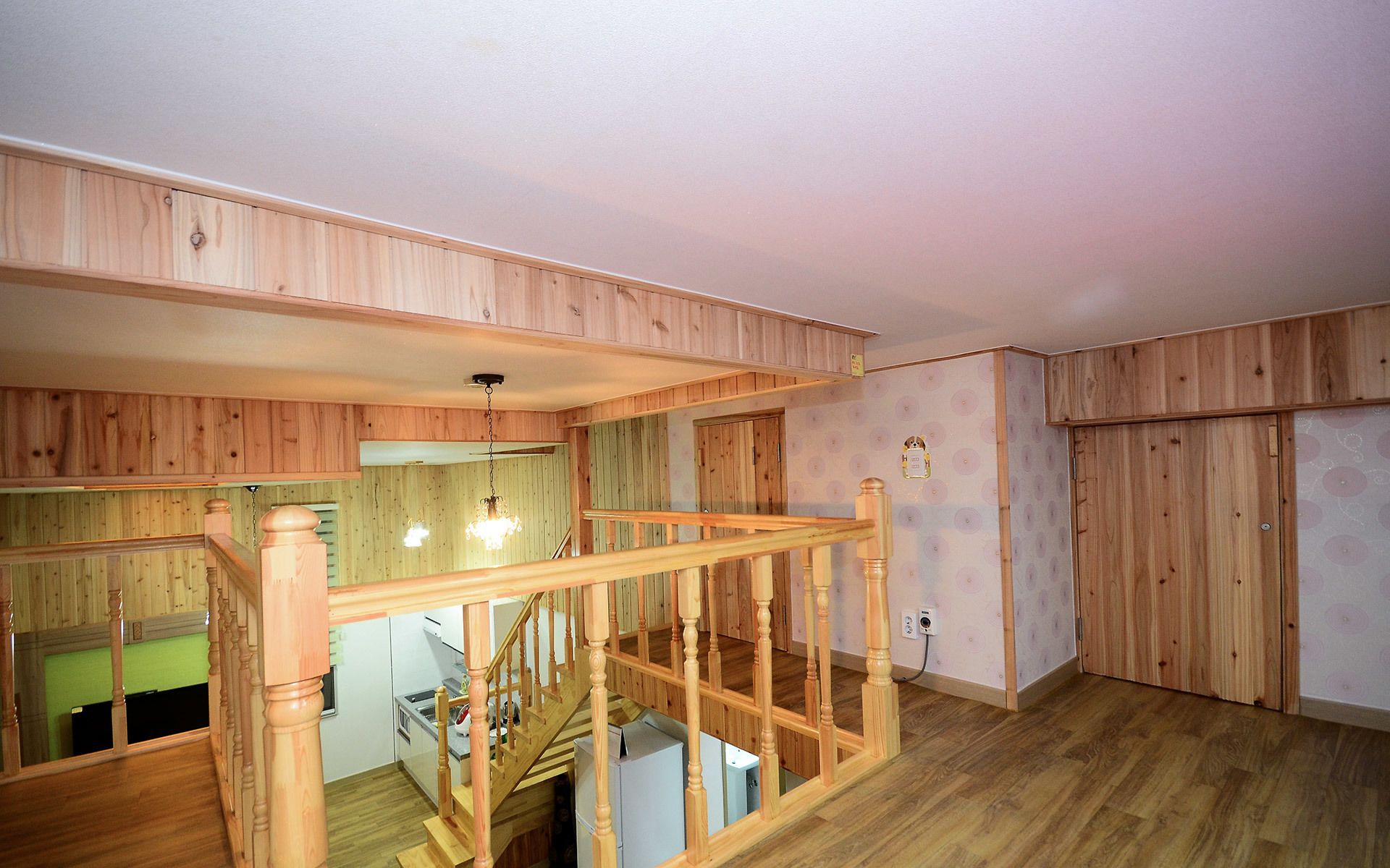 Een ruime kamer met houten lambrisering, een trap en een keukenhoek.