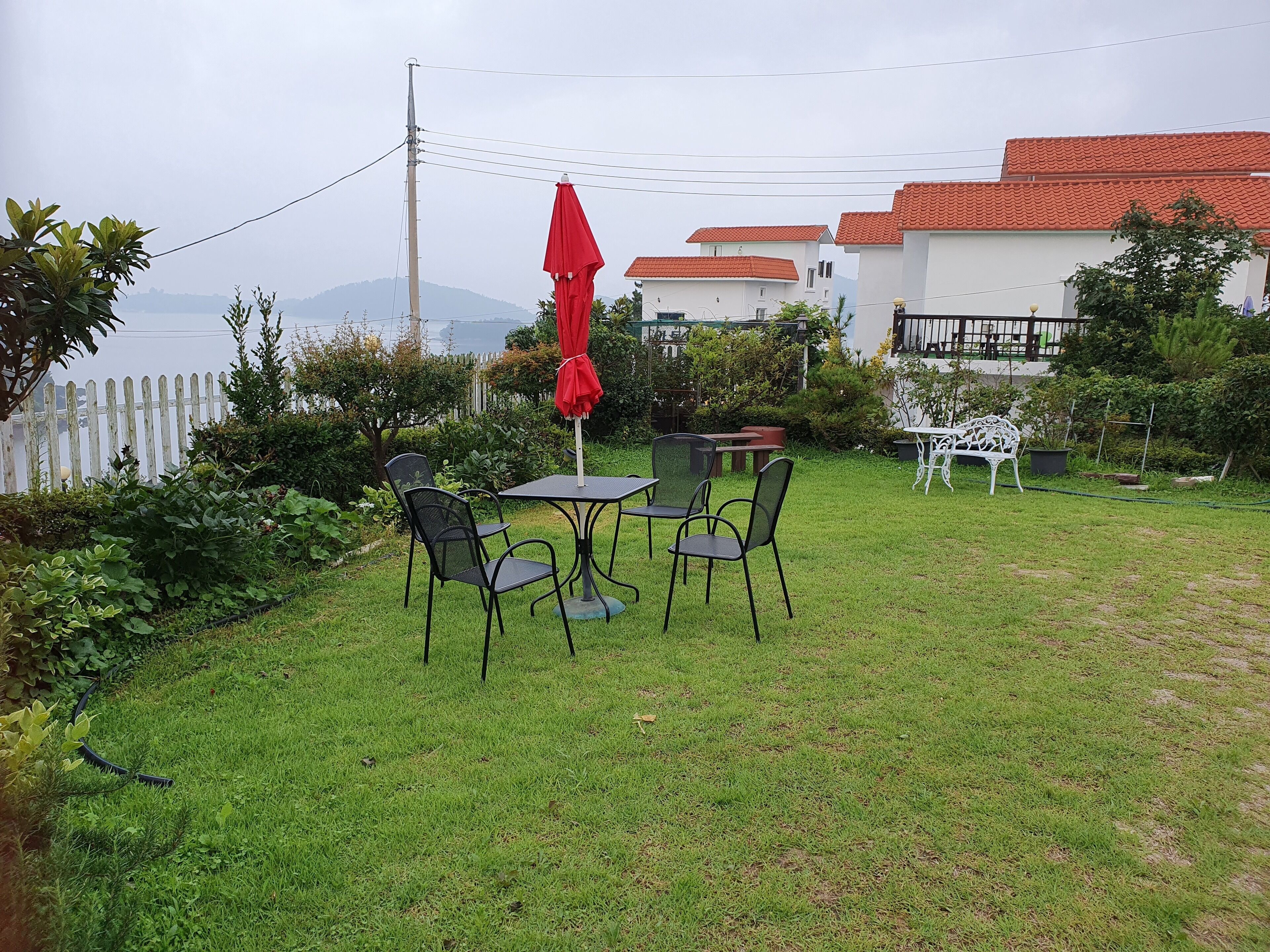 Un'area verde all'aperto con un tavolo e sedie, un ombrello rosso e un recinto bianco.