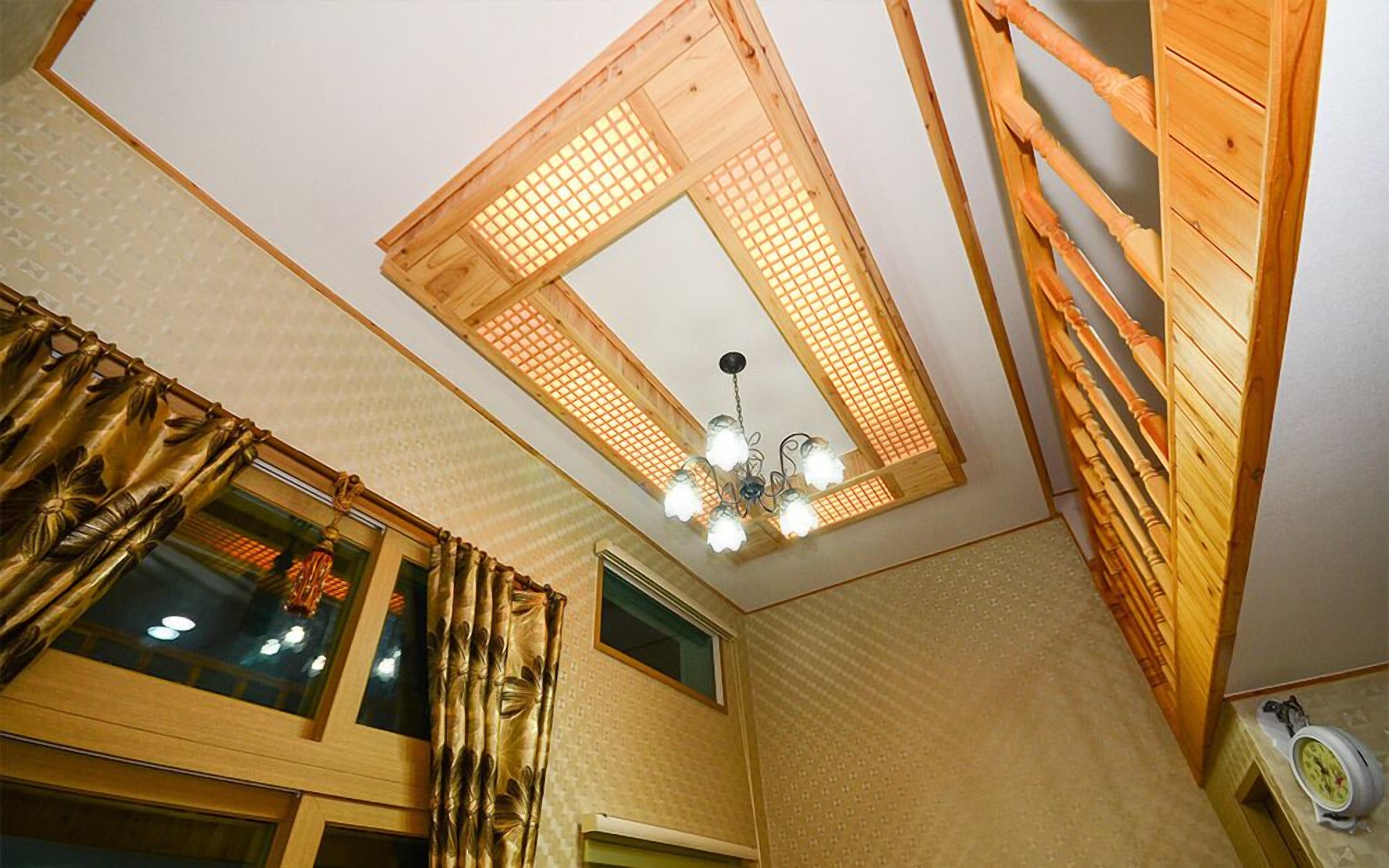Une pièce avec un plafond en pente, des poutres en bois, un lustre et une fenêtre avec des rideaux.