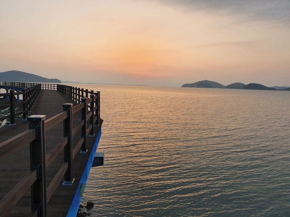 A wooden pier extending over calm water with a sunset in the background.