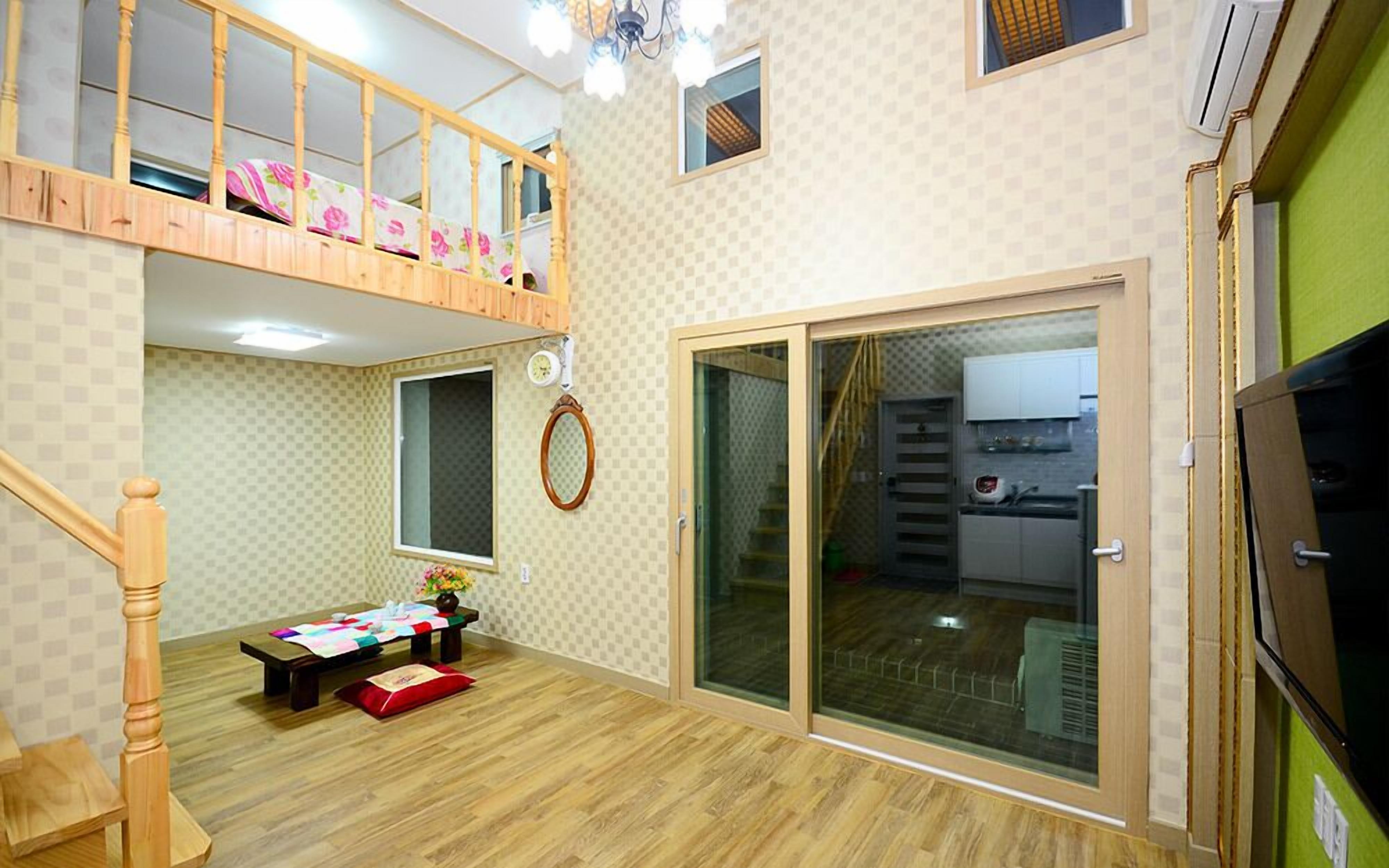 A spacious room with a wooden staircase, a dining area, and a sliding glass door leading to a kitchen.