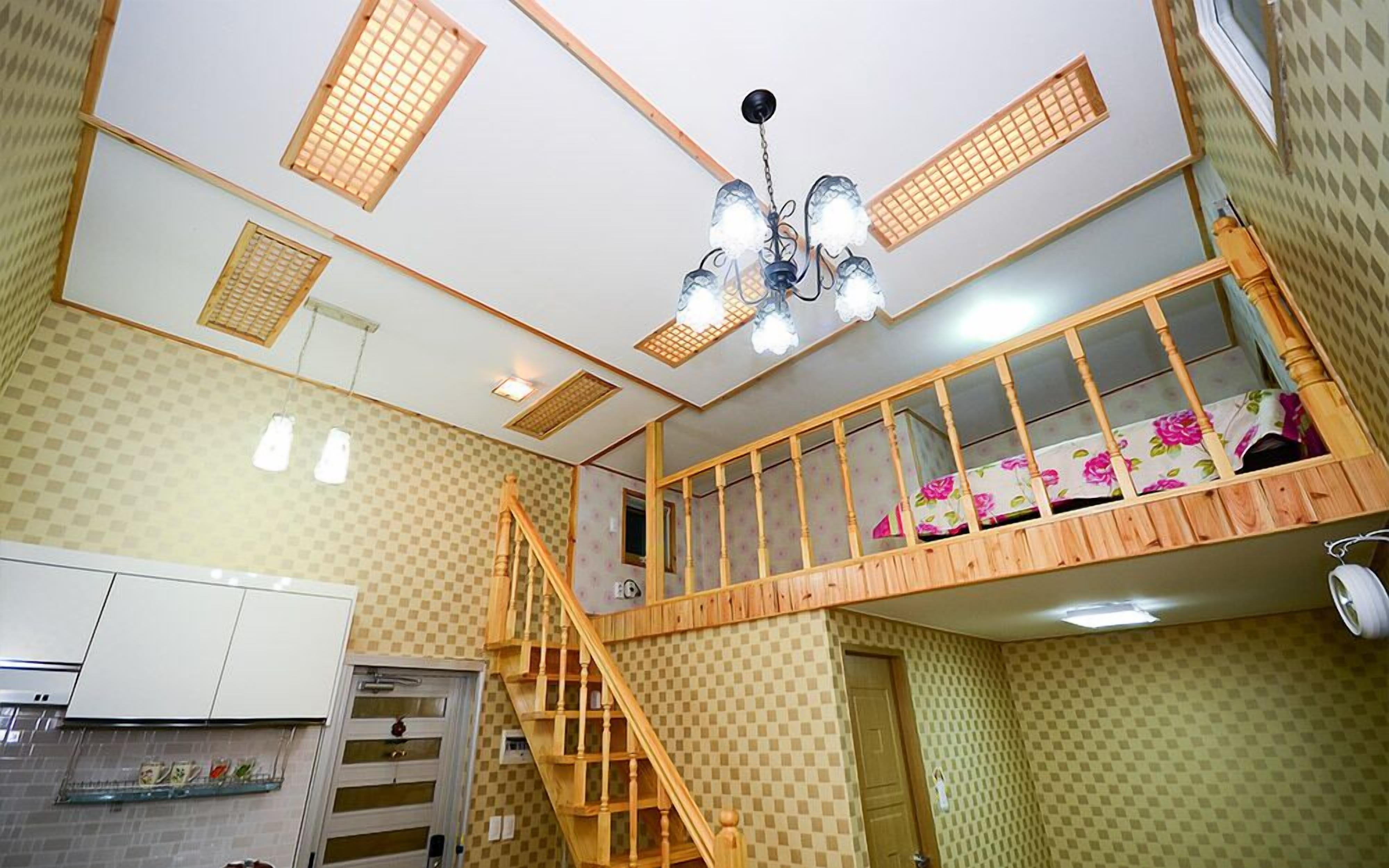 Een kamer met meerdere niveaus, een houten trap, een stapelbed en een keukenhoek.