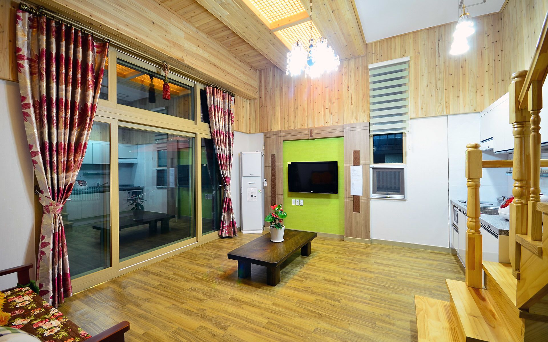 A modern living room with wooden flooring, a large sliding glass door, a flat-screen TV, and a green accent wall.