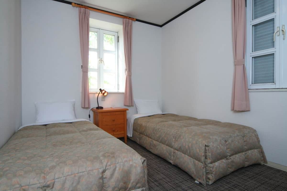 A room with two beds, a nightstand, a lamp, and a window with curtains.