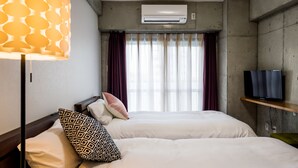 Quarto de hotel com duas camas, uma televisão e aparelho de ar condicionado.