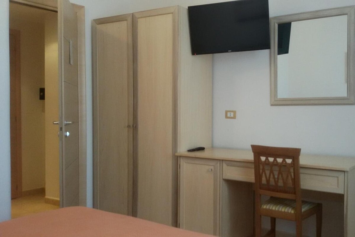 A room with a bed, a desk, a chair, a television mounted on the wall, and a wardrobe.