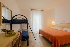 Una habitación con literas, un escritorio con frutero, una silla y una cama con colcha naranja.