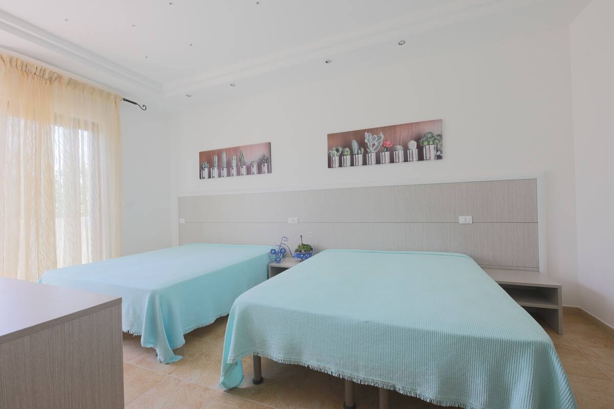 A hotel room with two single beds, a small bedside table with a plant, and a wall-mounted shelf with decorative items.