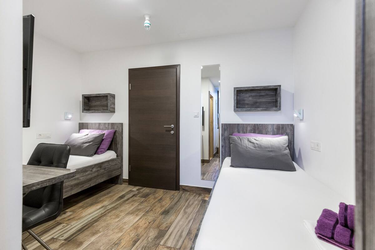 Une chambre d’hôtel moderne avec un plancher en bois, deux lits, un bureau et une chaise.