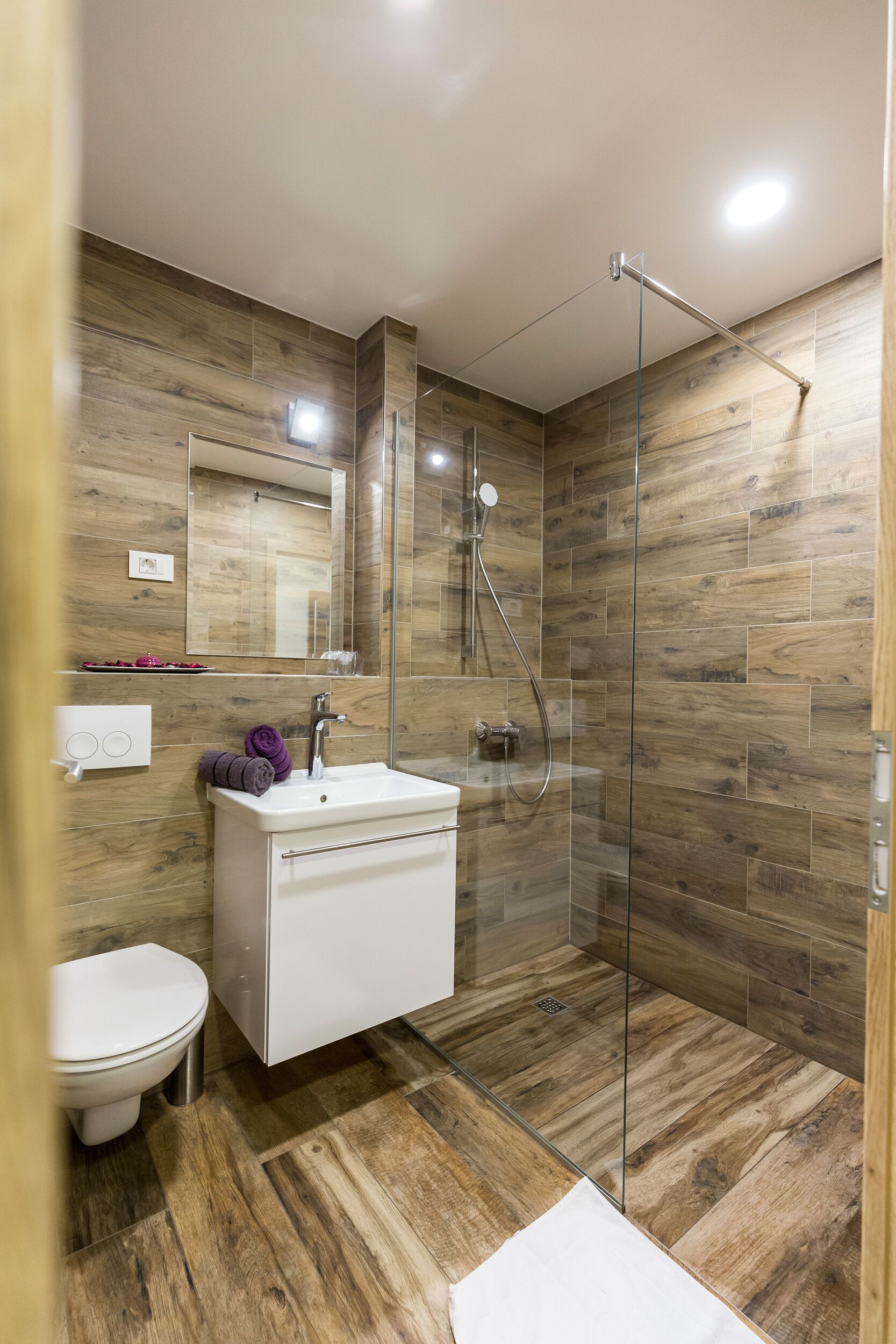 A modern bathroom with a glass-enclosed shower, a white sink, and a wooden floor.