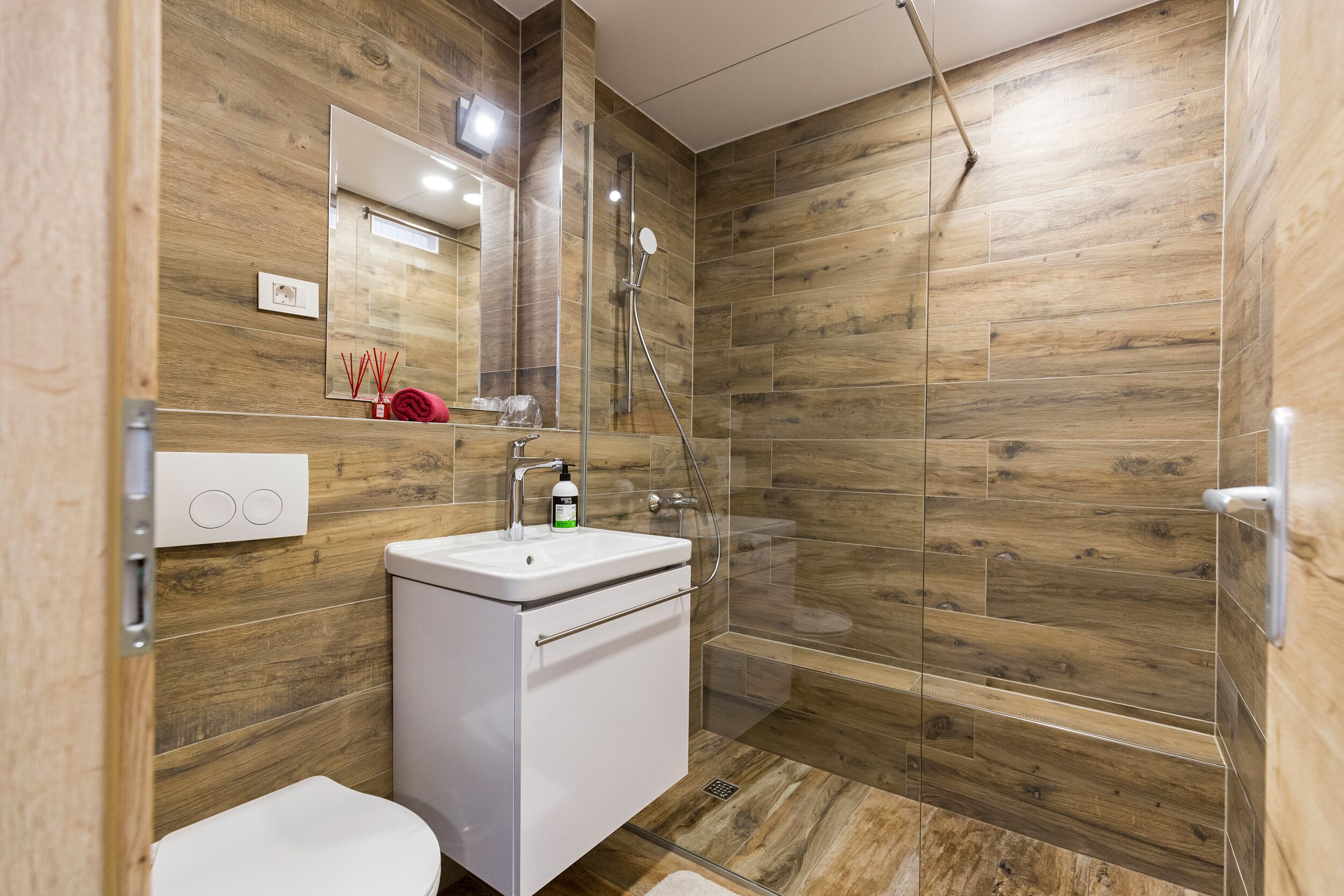 A modern bathroom with a wooden wall design, a glass shower enclosure, and a white sink.