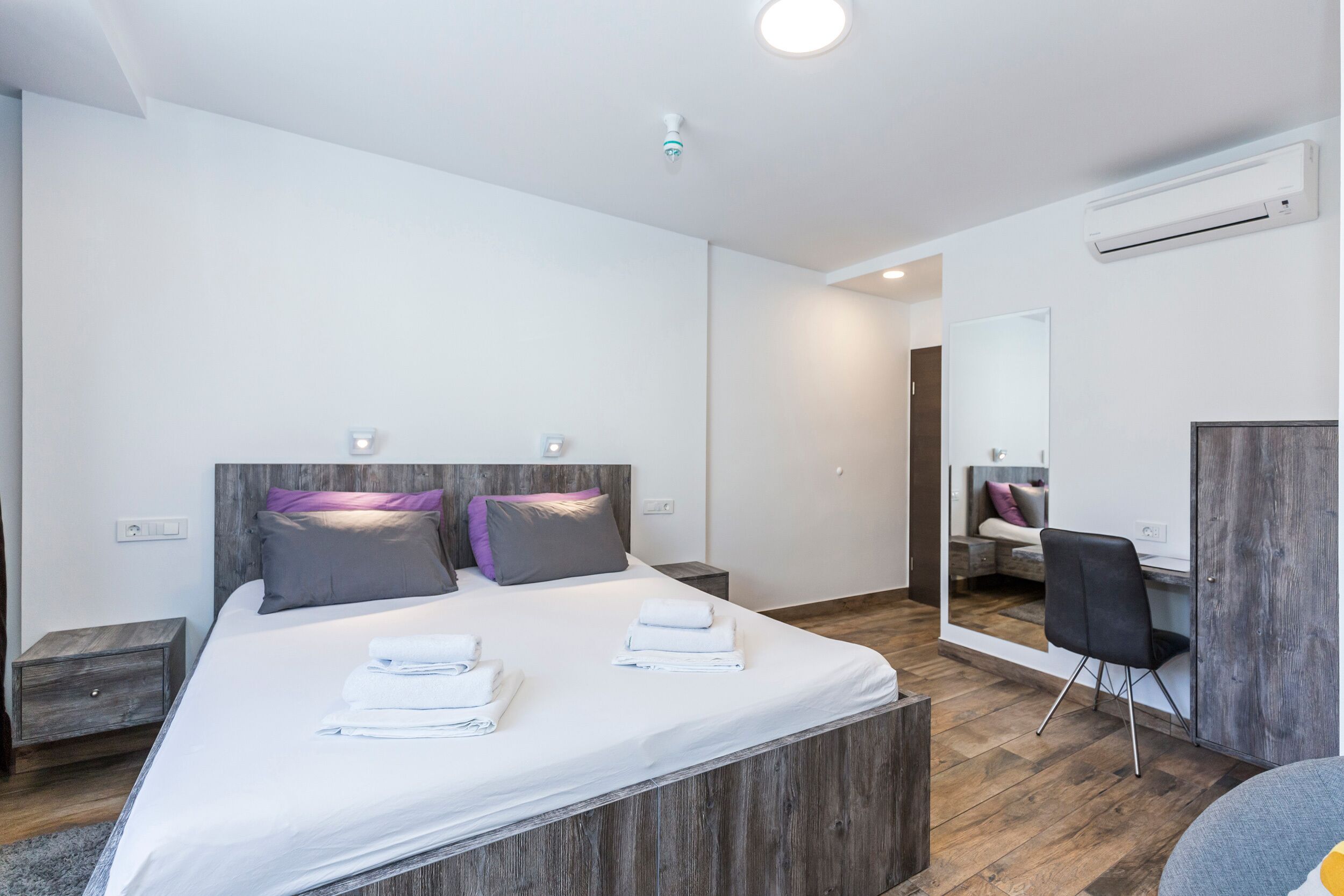 Quarto de hotel moderno com uma cama grande, cabeceira de madeira e uma escrivaninha embutida.