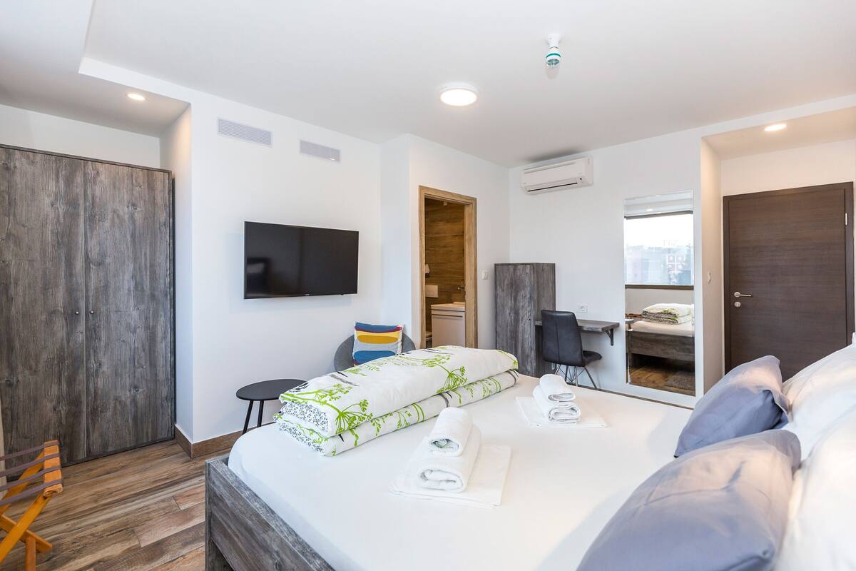 Une chambre d’hôtel moderne dotée d’un grand lit, d’un téléviseur à écran plat, d’une armoire en bois, d’un petit bureau et d’une fenêtre donnant sur la ville.