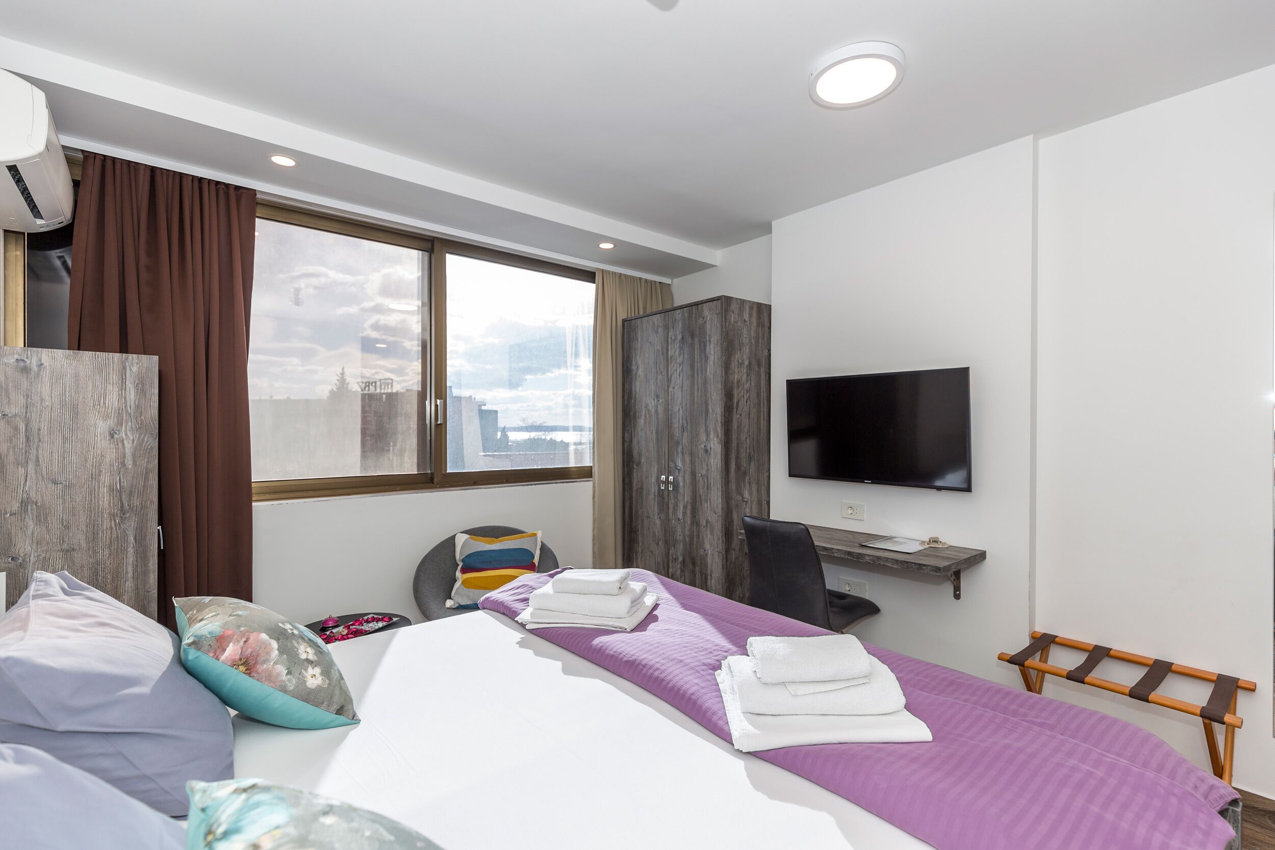 Ett modernt hotellrum med en säng, ett skrivbord, en TV och utsikt över staden.