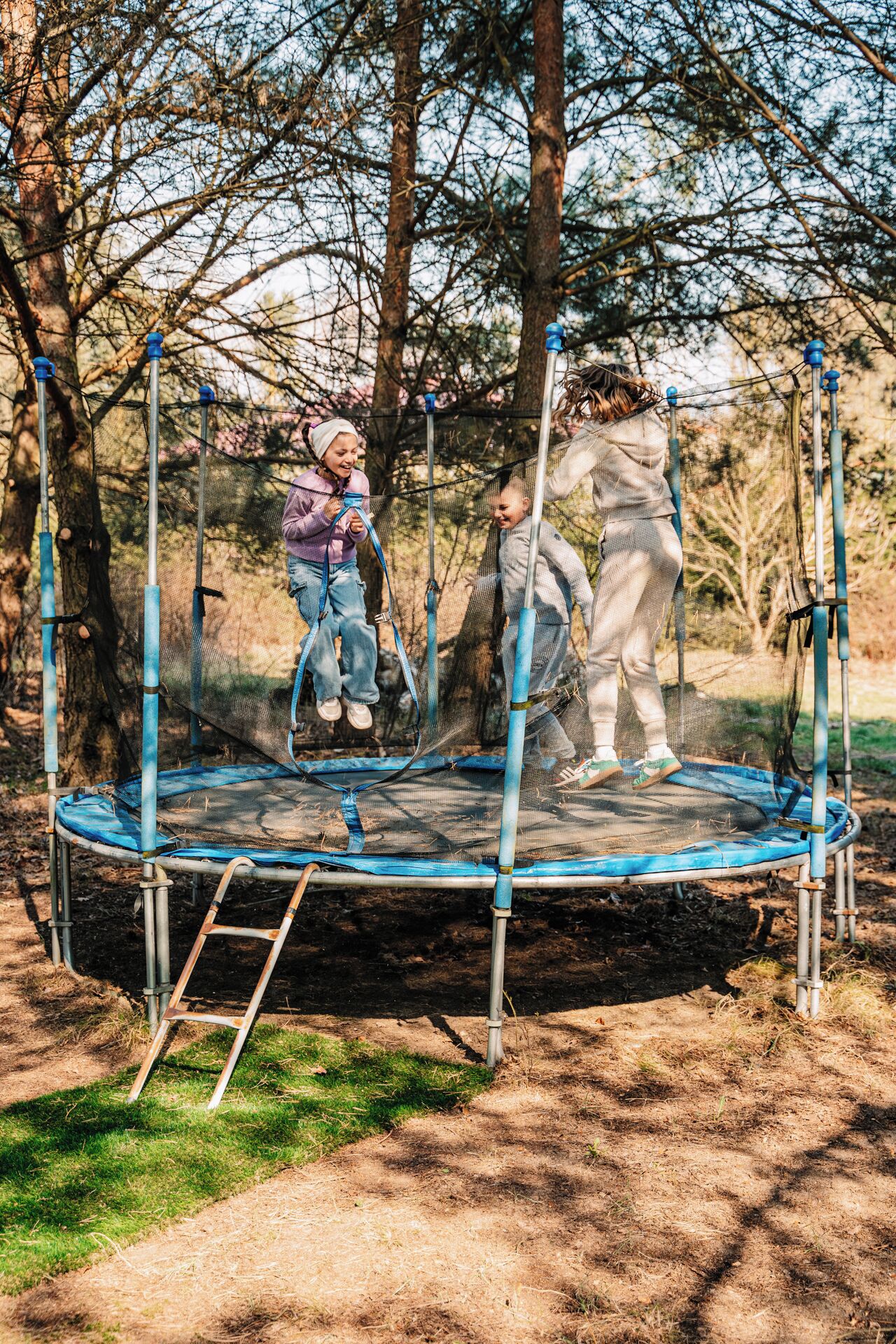 Un trampoline installé dans un espace boisé, avec des poteaux en métal et un filet de protection.