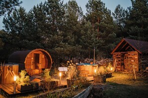 A rustic cabin with a curved wooden structure, a separate wooden building, and a well-lit deck area surrounded by trees. - Willa tuŻur (Osie)
