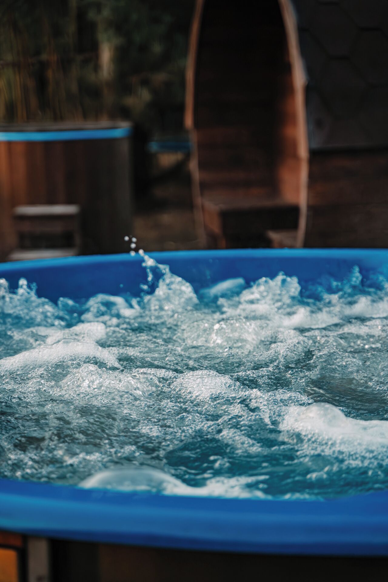 A hot tub with water splashing, a wooden barrel, and a blurred background.