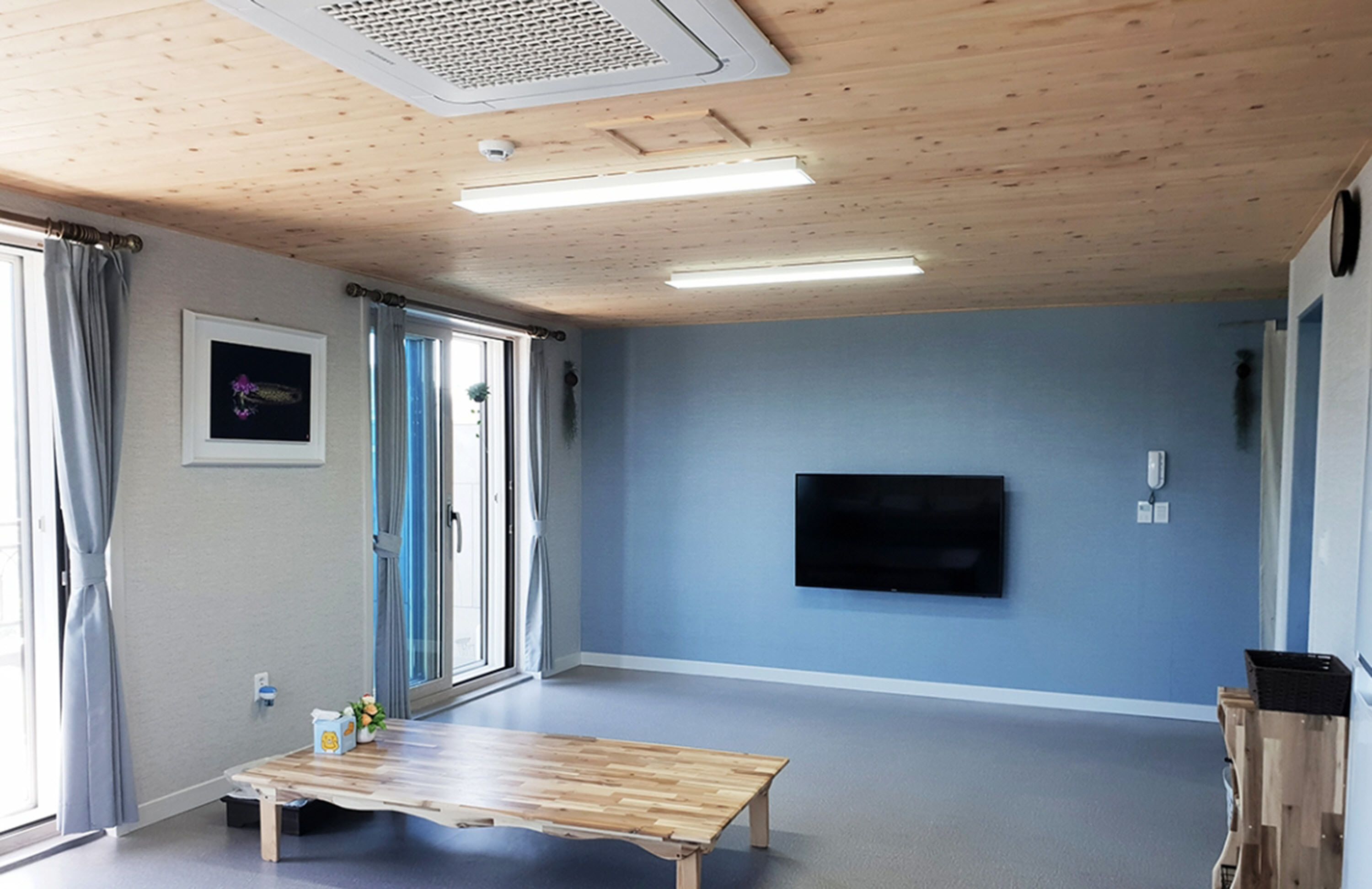 Una habitación con techo de madera, un televisor de pantalla plana montado en la pared, un banco de madera y una ventana con cortinas.