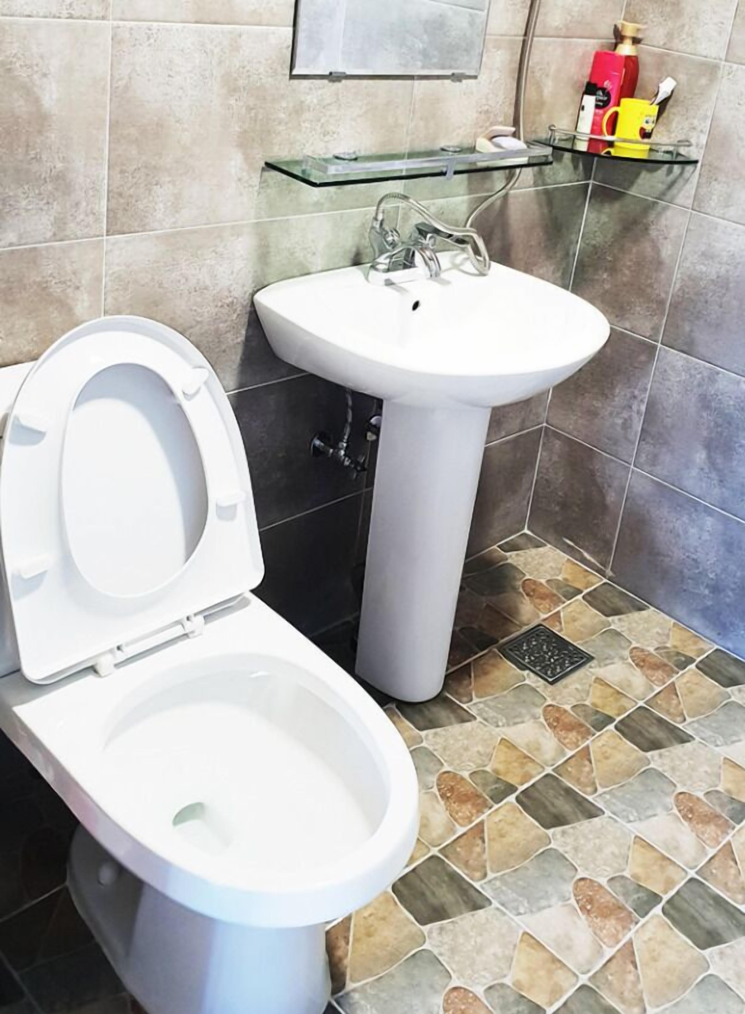 Un baño con inodoro, lavamanos y un estante de vidrio con artículos de aseo.