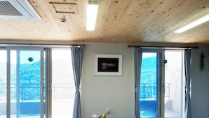 Ein Zimmer mit Holzboden, großen Schiebeglasfenstern zum Balkon, einem gerahmten Bild und einem kleinen Tisch mit einer Vase.