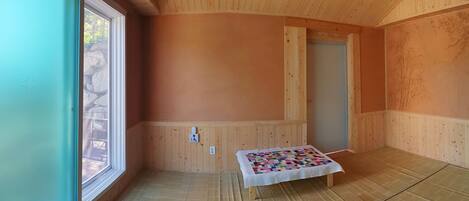 Una habitación con paredes y suelo de madera, una ventana, una puerta y un colcha en el suelo.