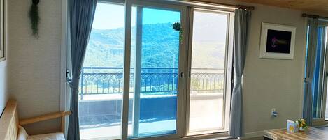 Una habitación con techo de madera, una puerta de vidrio corredera a un balcón, una pequeña mesa de madera y una cama con colchón blanco.