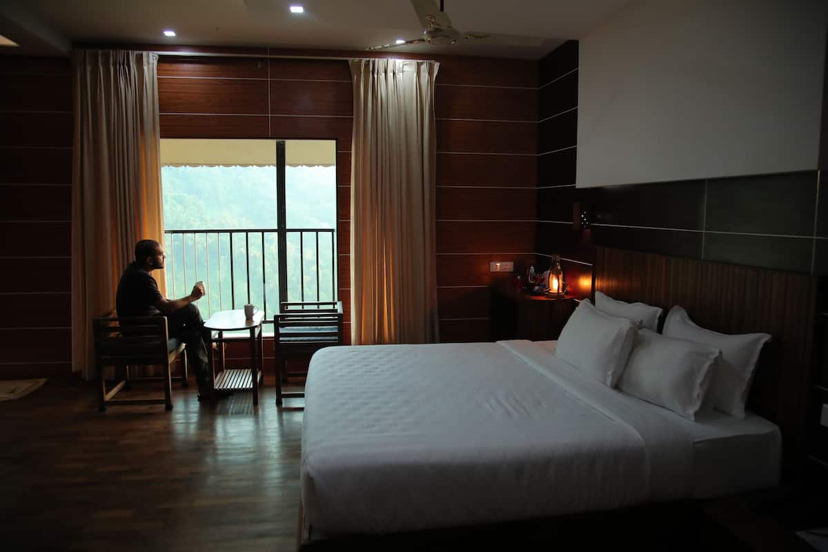 A hotel room with a large bed, a desk, and a chair. There is a window with curtains and a view of the outdoors.