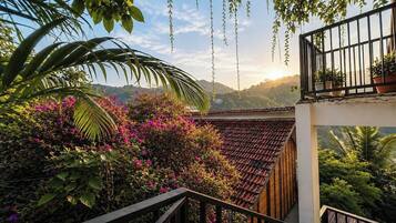A balcony with a view of a mountainous landscape, surrounded by lush greenery and flowering plants.