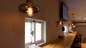 Un bar con mostrador de madera, luces colgantes y un ventanal con puerta.