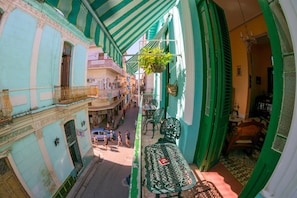 A narrow street with buildings on either side, a balcony with a table and chairs, and hanging plants. - Casa Colonial Tere (Havana)