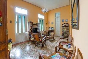 A spacious room with a tiled floor, wooden furniture, a chandelier, and a large mirror. - Casa Colonial Tere (Havana)