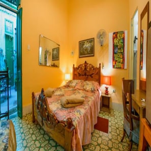 A bedroom with a wooden bed, a small bedside table, a chair, a fan, and a door leading outside. - Casa Colonial Tere (Havana)