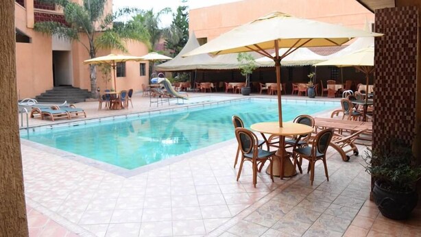 Un área de piscina con suelo de baldosas, sillones de descanso y sombrillas.