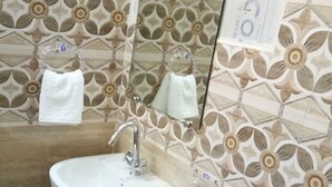 Une salle de bain avec un lavabo blanc, un miroir et un porte-serviettes. Le mur est décoré de carreaux à motifs floraux.