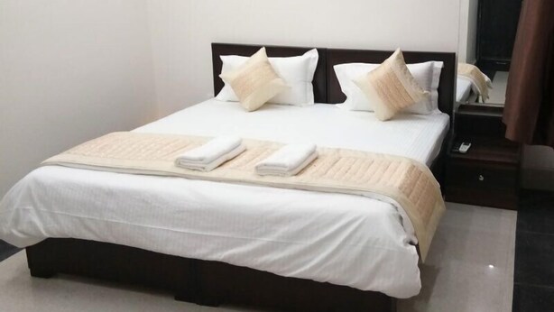 Un lit bien fait, avec du linge de lit blanc et un plaid beige, une table de chevet avec un téléphone et un miroir au mur.