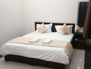A neatly made bed with white linens and a beige throw blanket, a bedside table with a phone, and a mirror on the wall. - A1 Guest House (Gurugram)