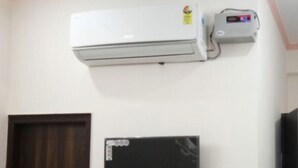 Une pièce avec un climatiseur blanc, un petit appareil électronique fixé au mur et un téléviseur noir monté sur le mur.